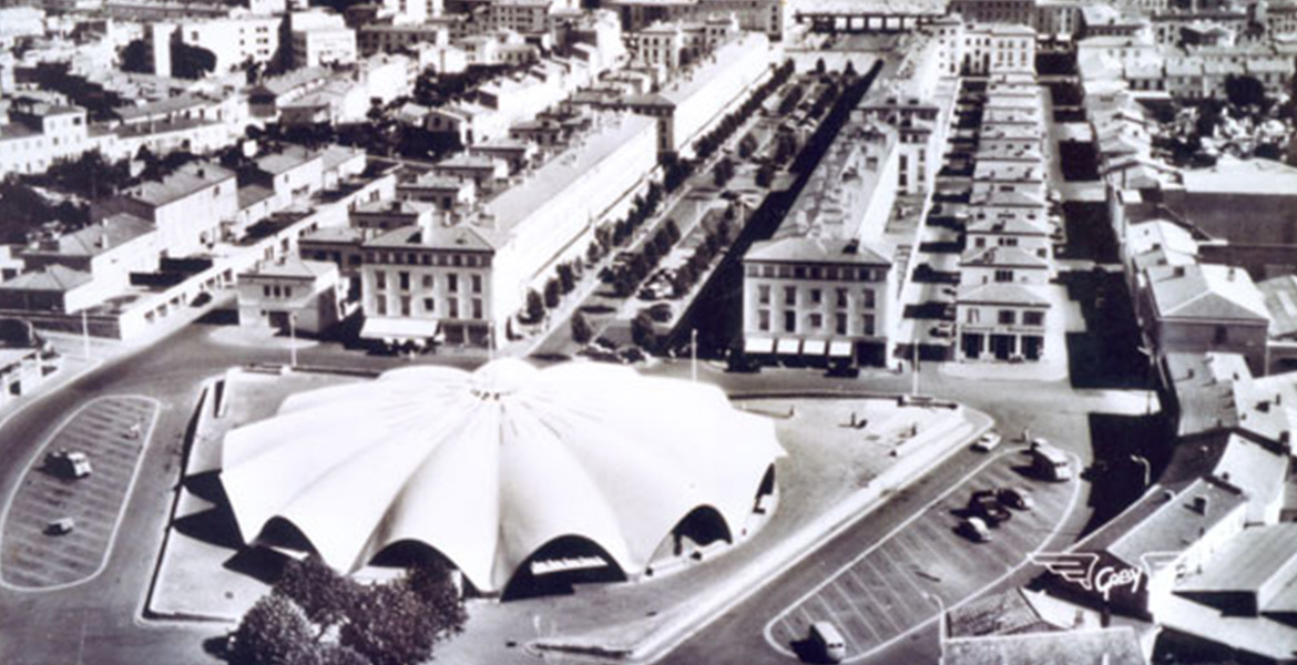 Vue aérienne du marché central de Royan, en forme de coquillage, entouré de bâtiments résidentiels et de rues structurées.