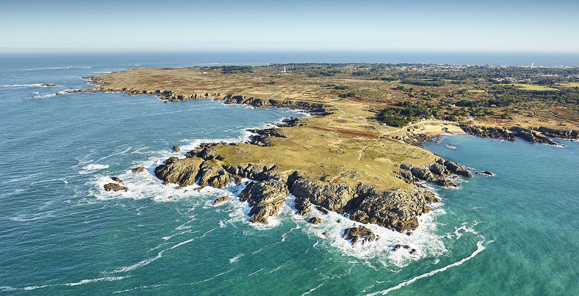 Vue aérienne d'une côte rocheuse de l'Île d'Yeu entourée par l'océan, avec des étendues de terre verdoyantes et des sentiers.