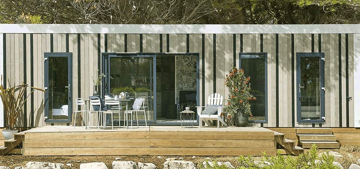 Un mobil-home moderne en bois de la gamme Signature avec une grande terrasse, entourée de rochers et de verdure.