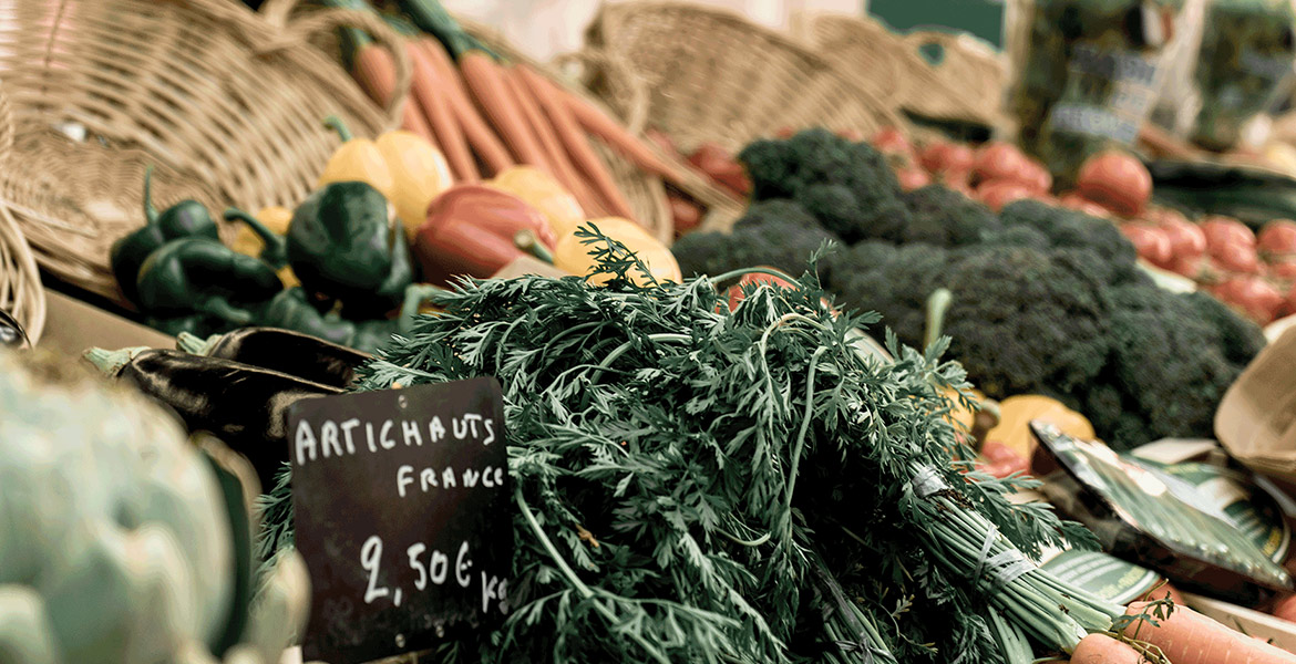 Un étal de marché avec une variété de légumes frais, dont des carottes, des poivrons, et du brocoli, avec une pancarte indiquant le prix du légume.