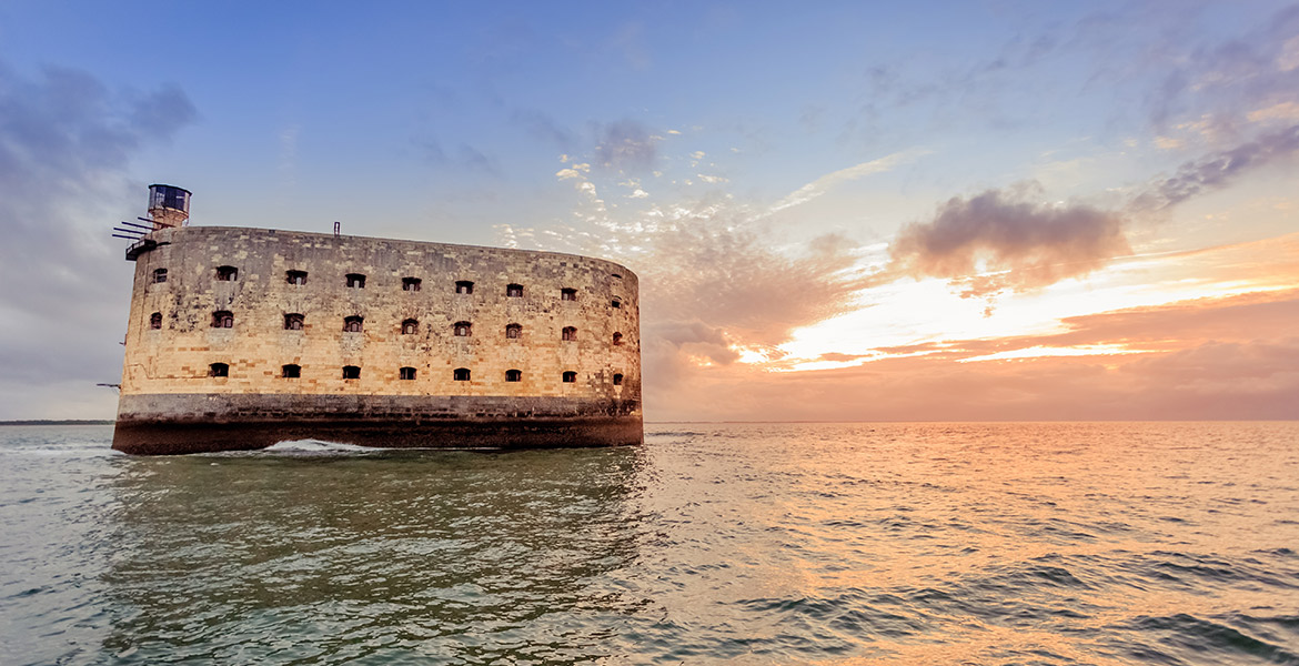 Fort Boyard, situé au milieu de l'océan en Charente-Maritime, éclairé par un coucher de soleil aux teintes orangées et roses.