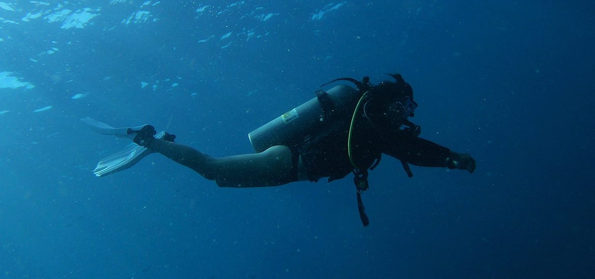 Un plongeur en combinaison de plongée sous-marine nageant dans les eaux bleues profondes.