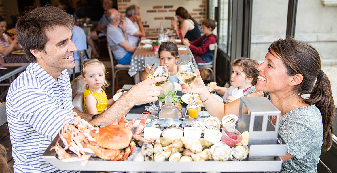 Un couple avec des enfants partageant un repas de fruits de mer dans un restaurant aux Sables d'Olonne, trinquant avec des verres de vin blanc.