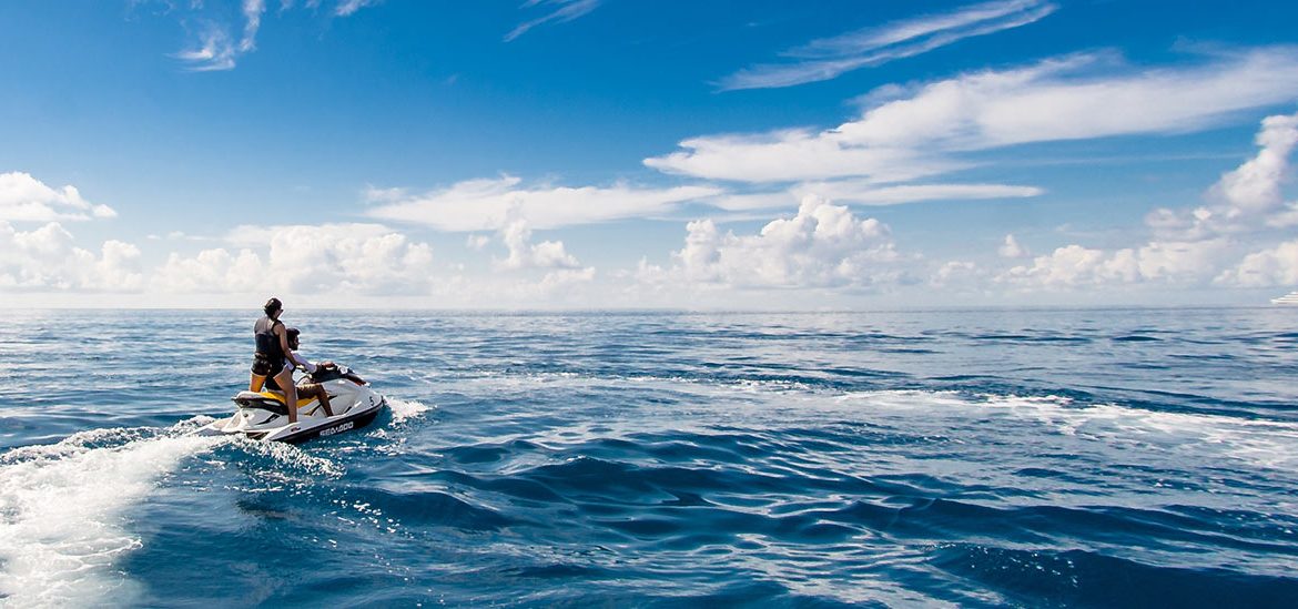 Personne faisant du jet-ski sur une mer bleue sous un ciel dégagé avec quelques nuages.