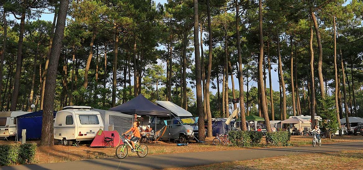 Des campeurs avec des tentes et des caravanes installés dans le Camping Campéole Plage Sud, certains faisant du vélo sur les sentiers.