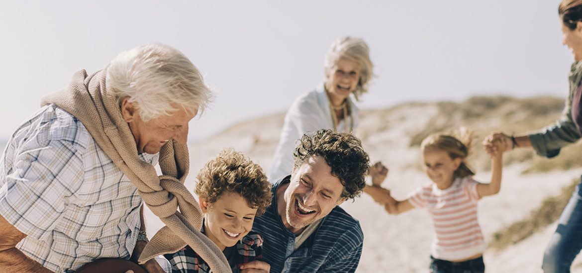 Une famille s'amusant sur une plage ensoleillée. Un grand-père tient un ballon tandis que ses petits-enfants essaient de l'attraper, sous le regard souriant des parents.