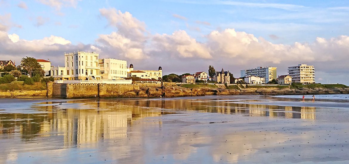 Plage de pontaillac, avec vue sur les hôtels de bord de mer sous une lumière ensoleillée de couché de soleil.