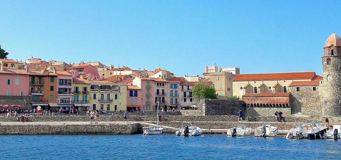 Vue du port de Collioure avec ses maisons colorées en arrière-plan et l'église Notre-Dame-des-Anges au bord de l'eau.