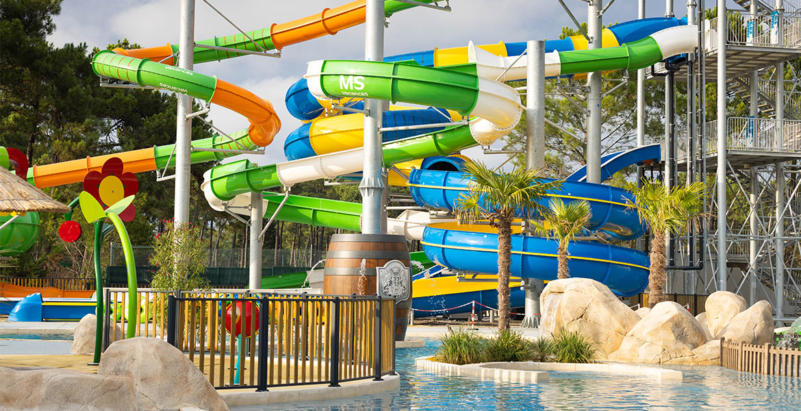 Toboggans aquatiques colorés entourés de palmiers dans un parc aquatique, avec une petite piscine au premier plan.