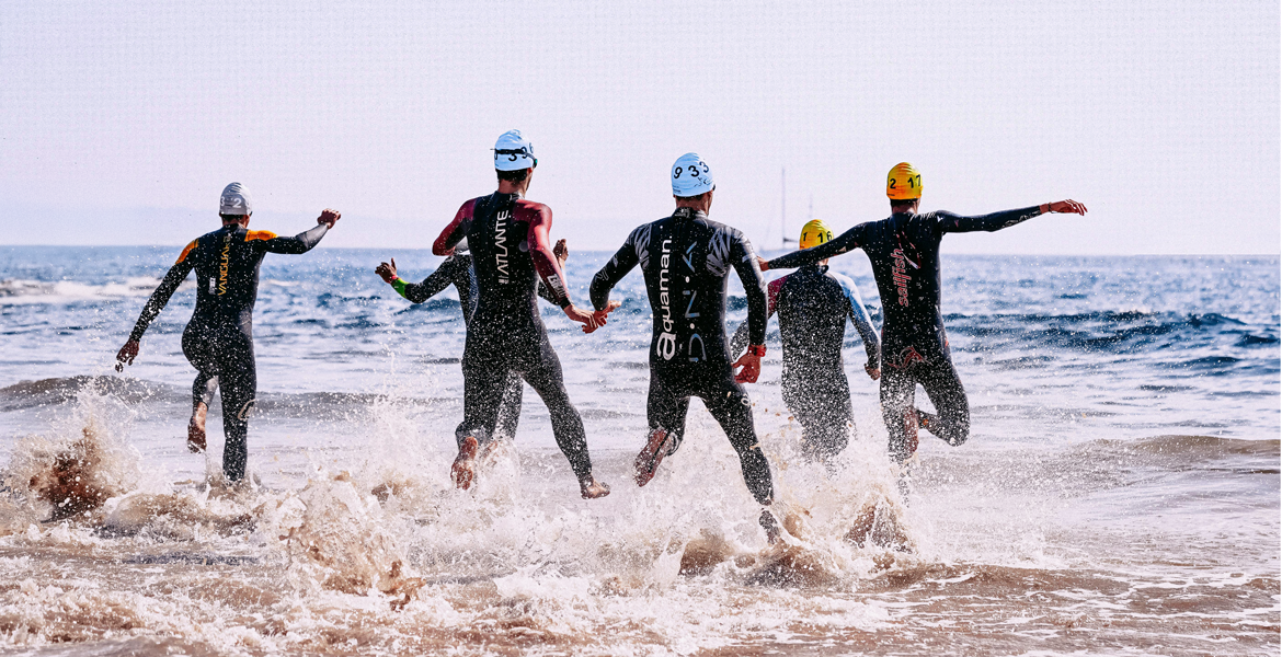 Un groupe de triathlètes participant à l'Ironman des Sables d'Olonne. Les vagues éclaboussent autour d'eux alors qu'ils s'élancent vers la mer.